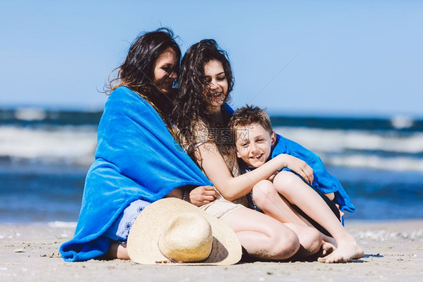 母亲和子女坐在沙滩上裹着毯子图片