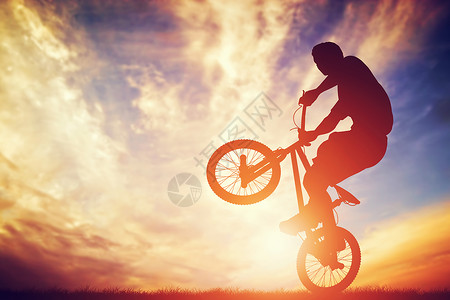 骑自行车的男子在日落天空上玩把戏图片