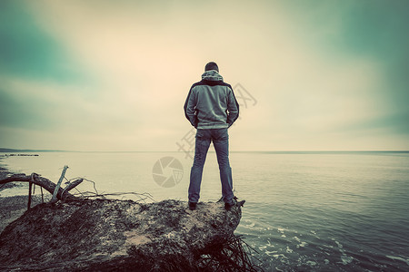 中年男子站在荒野海滩上的破树望远海平线传统概念背景图片