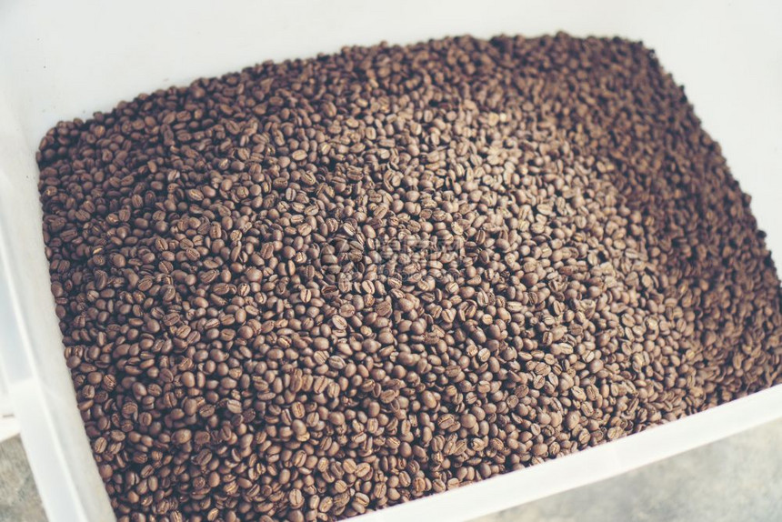 新鲜的烤咖啡豆从一个大型的咖啡烘烤机上倒入冷却气瓶豆子上的动作模糊不清图片