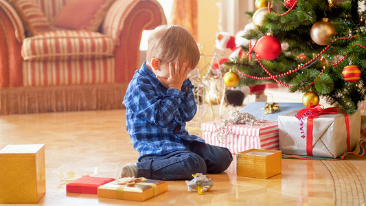 小男孩坐在圣诞树下哭泣图片
