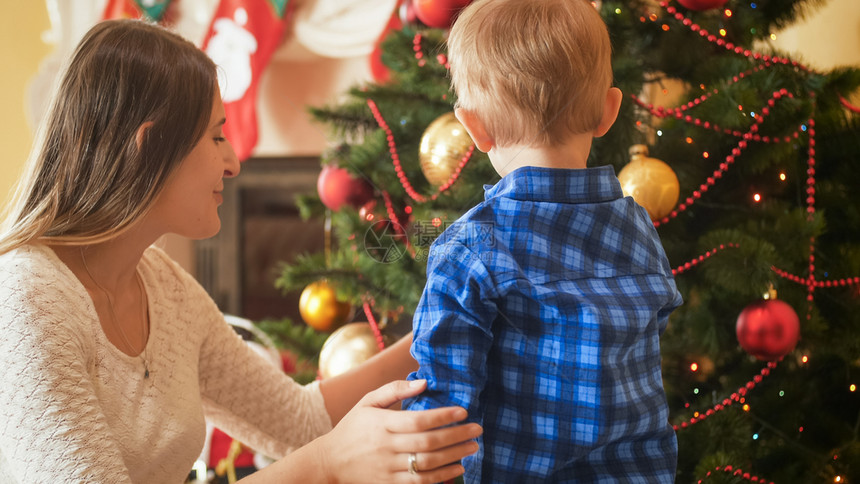 在客厅的圣诞树旁边小男孩与母亲站在一起图片