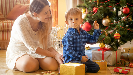 微笑的母亲看着她小男孩拿着圣诞礼物快乐的微笑母亲看着她小男孩图片