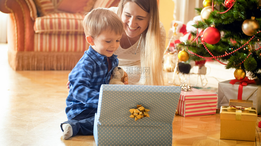 欢笑的男孩坐在圣诞树下面打开礼物盒图片