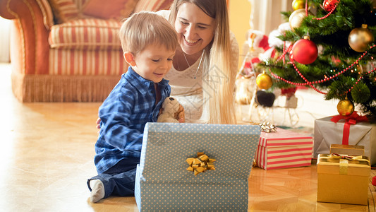 欢笑的男孩坐在圣诞树下面打开礼物盒背景图片