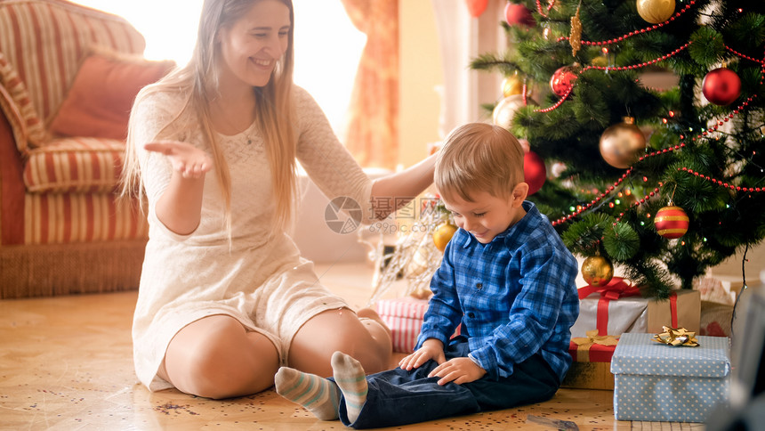 快乐的妈与幼儿男孩坐在旁边圣诞树的早晨快乐笑妈肖像图片