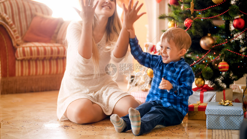 欢笑的小孩男在圣诞节早上和妈一起扔彩色蛋白圣诞早晨快乐的笑小孩男和妈一起扔彩色蛋白图片