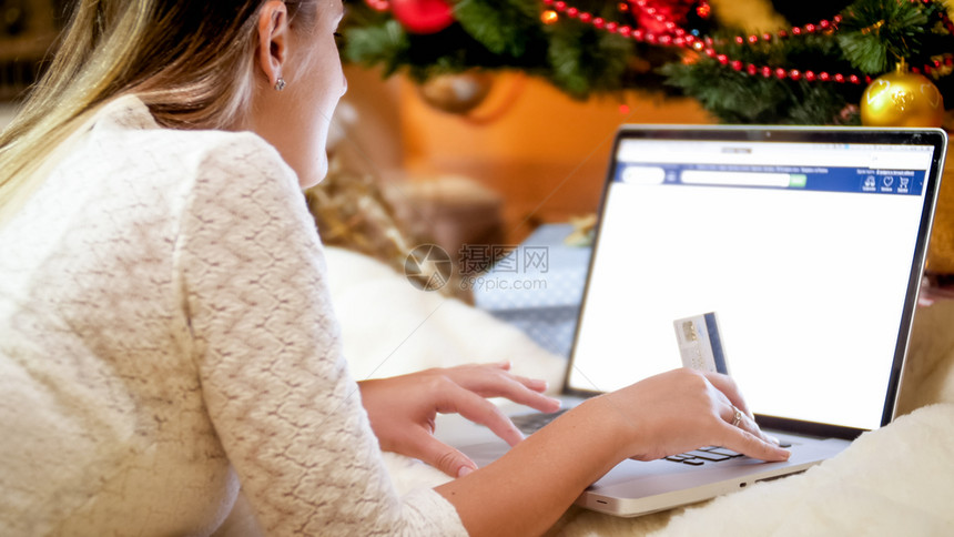 在圣诞树下面有信用卡的年轻女子特查照片她躺在圣诞树下面为冬季假日订购礼物图片