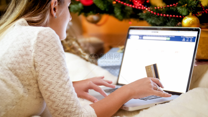 拥有笔记本电脑的妇女躺在圣诞树下浏览上线商店拥有笔记本电脑的年轻妇女躺在圣诞树下浏览上线商店图片