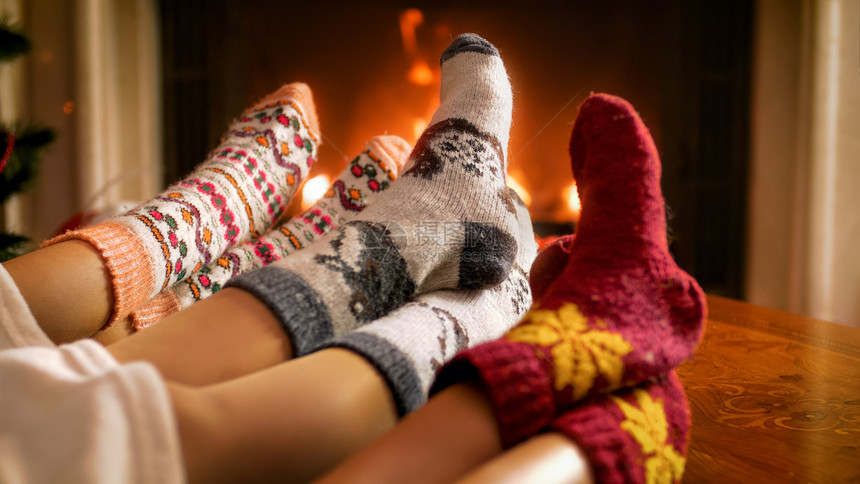 穿着毛绒袜子的年轻家庭在毛毯下躺着燃烧的火焰中变暖图片