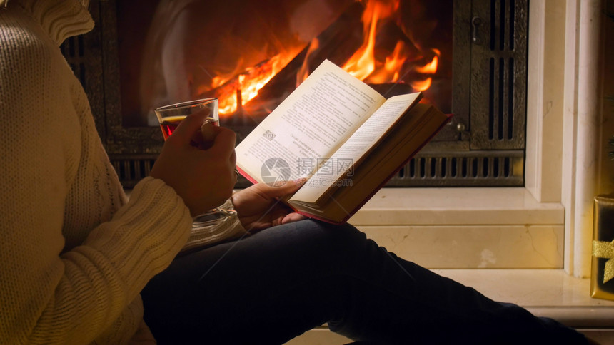 妇女晚上在壁炉边喝茶和阅读书青年妇女晚上在壁炉边喝茶和阅读书图片