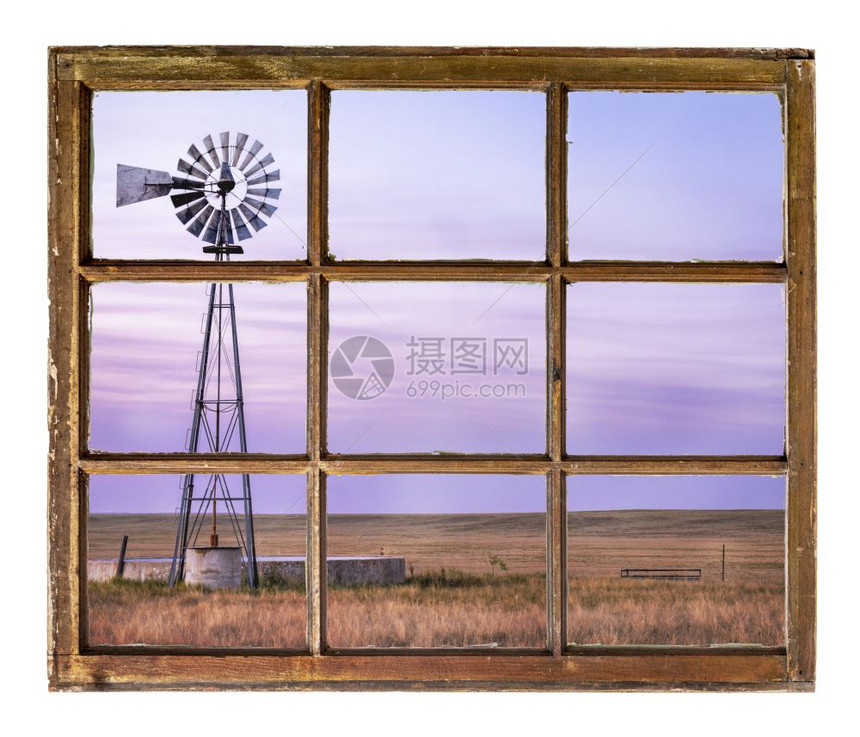 黄昏的草原上装有泵水和牛池的风车从一个古老的小木屋窗户看到图片