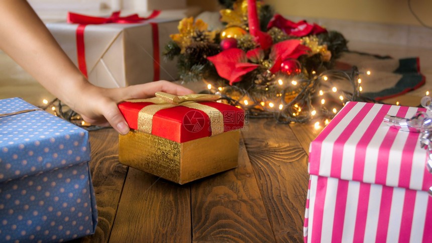 女手在木地板上把礼物放在圣诞树下面的盒子里图片