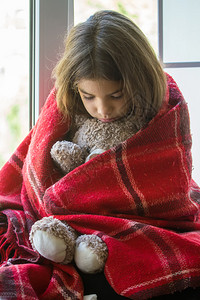 坐在窗台上的可怜小女孩躲在一个老的格子后面仔细地拥抱着她可爱的玩具熊图片