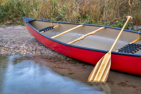 在湖岸上用木板划桨的红色独木舟图片