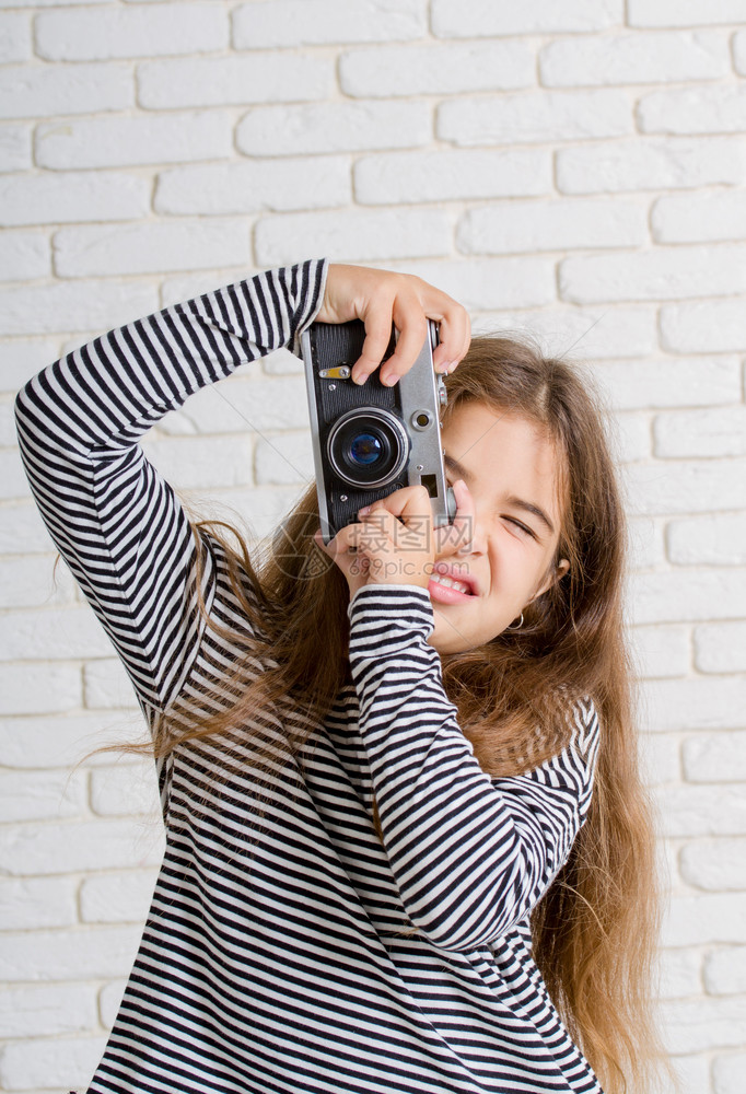 身穿条纹上衣反光照相机的小女孩在轻砖墙附近拍照图片