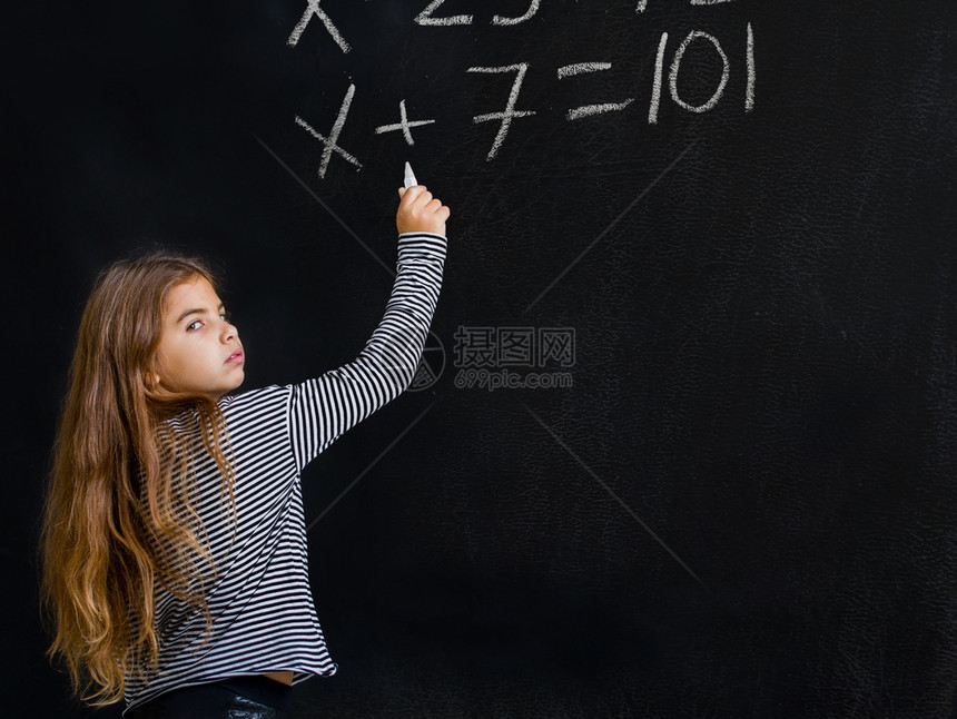 一个小女孩站在学校董事会旁边试图解决她数学上的一个困难任务图片