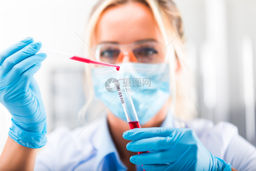 在保护眼镜面具和手套中年轻有吸引力的集中女科学家她们将红色液体物质和管子放在科学化实验室中图片