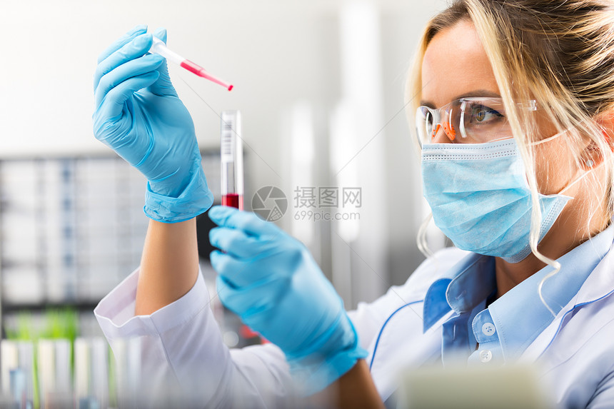 在保护眼镜面具和手套中年轻有吸引力的集中女科学家她们将红色液体物质和管子放在科学化实验室中图片