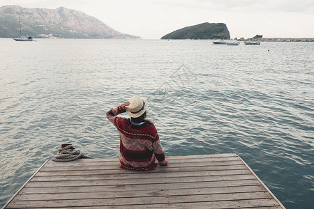 亚速尔群岛戴帽子的年轻女孩坐在木码头上看着地平线戴帽子的年轻女孩坐在木码头上看着地平线背景
