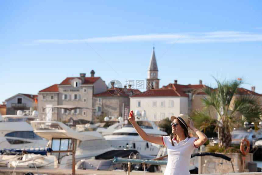 戴帽子的年轻旅行女青在夏季阳光明媚的地中海城市拍摄自照片并配有智能手机相图片