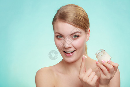 美容治疗女在脸上涂润湿奶油持有皮肤护理产品的罐子工作室拍摄绿色蓝底女在皮肤上涂奶油背景图片