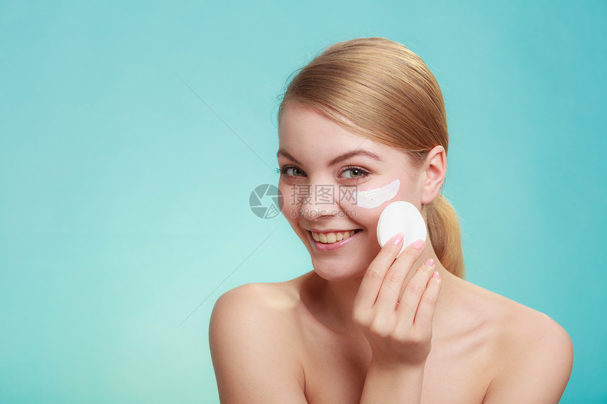 妇女用棉布垫子从脸上抹去化妆品年轻女孩照顾皮肤护理概念工作室拍摄在蓝色上妇女用奶油和棉垫擦除化妆品图片