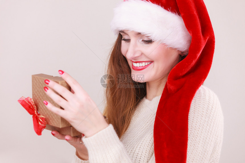 穿着圣达克萨斯帽子的开心女人着红弓的金礼盒圣诞节时间赠与和幸福的概念女人开礼物盒图片