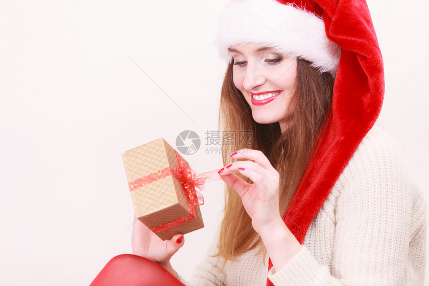 穿着圣达克萨斯帽子的开心女人着红弓的金礼盒圣诞节时间赠与和幸福的概念女人开礼物盒图片