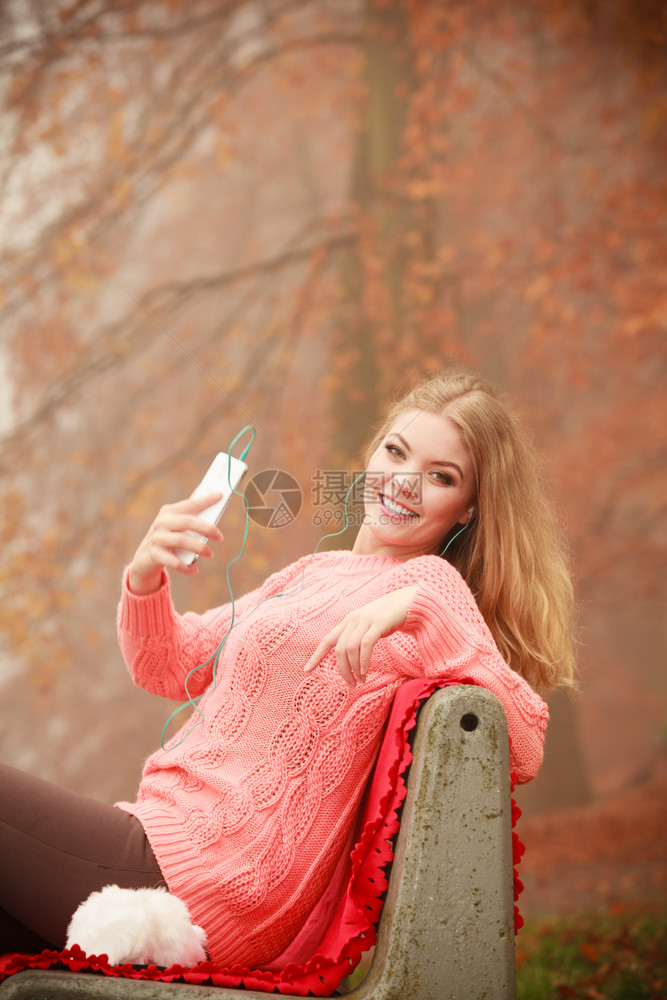 数字设备外面的学生带手机年轻女坐在公园长椅上的迷人女孩秋季天气带手机的年轻女图片
