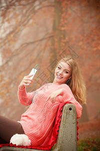 数字设备外面的学生带手机年轻女坐在公园长椅上的迷人女孩秋季天气带手机的年轻女背景图片