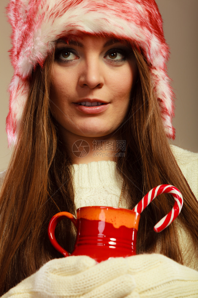 圣诞时间概念穿着毛皮帽子的很贴心女人拿着红杯子喝饮料甜的甘蔗带着杯子和甘蔗的圣诞女孩图片
