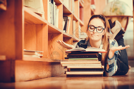 在学校教育概念中身戴眼镜的聪明女学生孩躺在大图书馆的地板上阅读书本图片