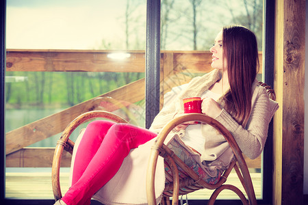 在家里坐摇椅上着舒适的年轻女士坐在摇椅上窗前客厅休息享受咖啡或茶饮图片