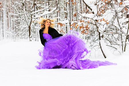 穿着长紫色裙子的金发年轻美女在雪的冬季森林或户外的木里背景图片
