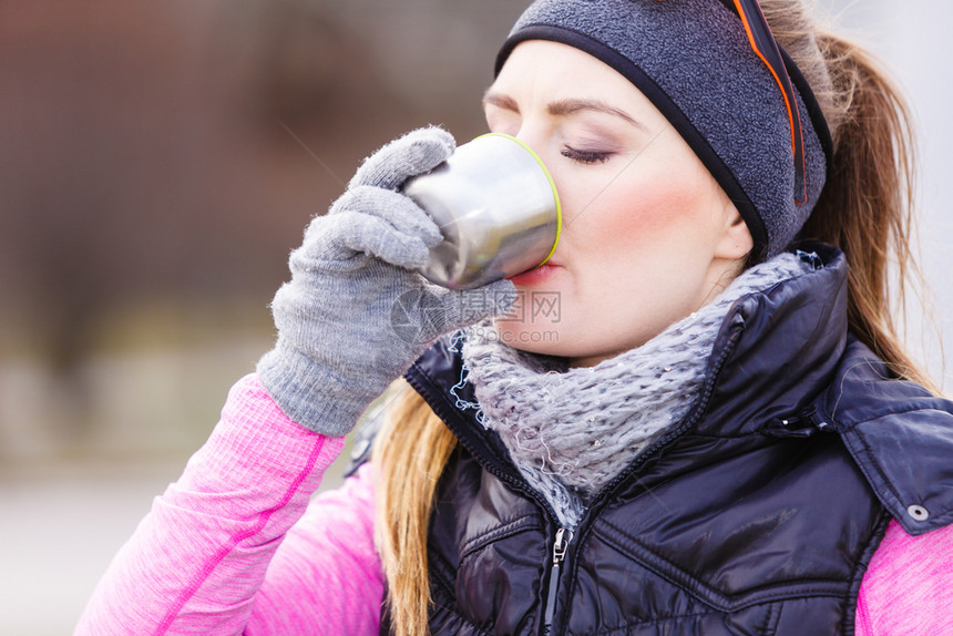 女旅行者在寒冷的天气中穿着温暖运动服装在户外穿着温暖运动服装的女旅行者在寒冷的天气中喝着从真空瓶子热水中取出的茶暖和起来图片