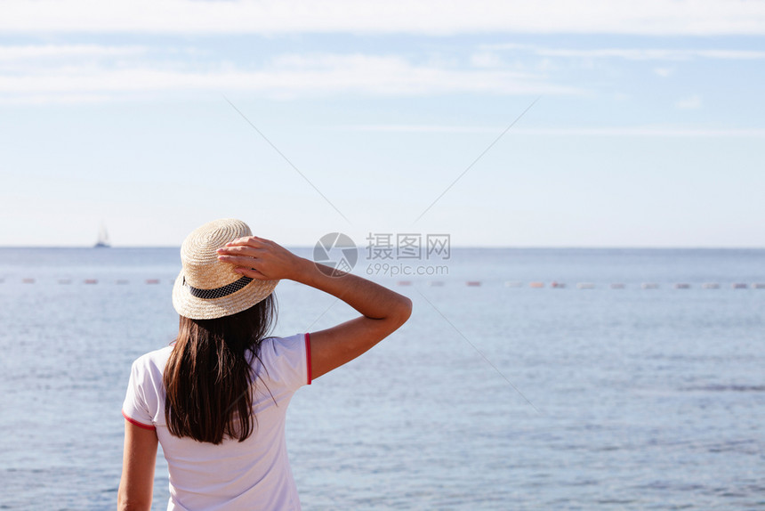 美丽的女孩看着海戴帽子的年轻女孩看着平静的海面图片