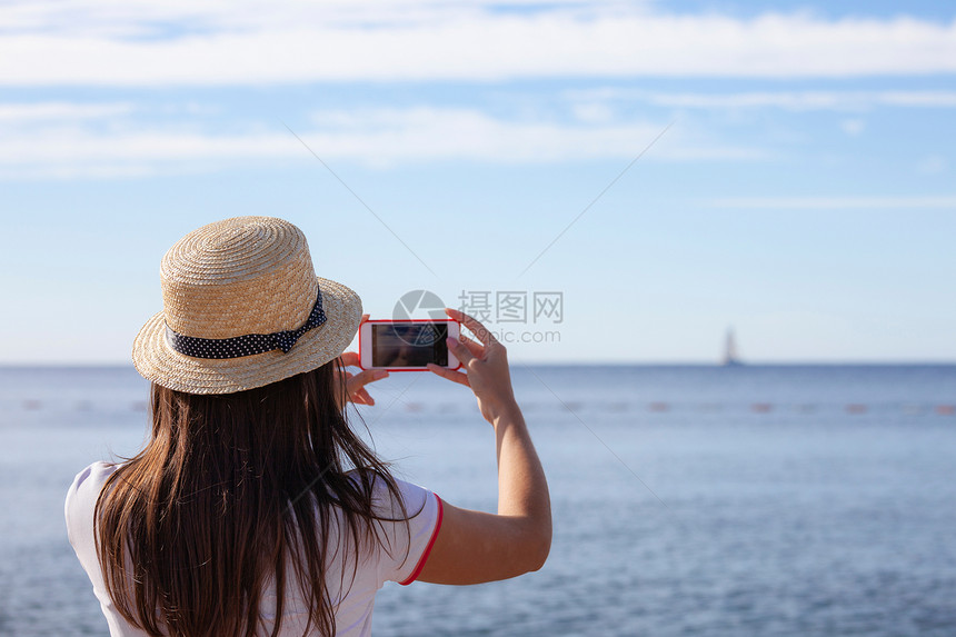 戴帽子的年轻女旅行者用智能手机照相拍摄夏季阳光明媚的海景照片Brunette女孩在暑假拍摄照片黑山布德瓦戴着帽子的年轻女旅行者用图片