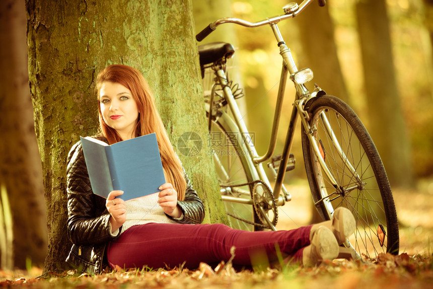 树下红发女人坐在自行车旁边阅读书籍图片