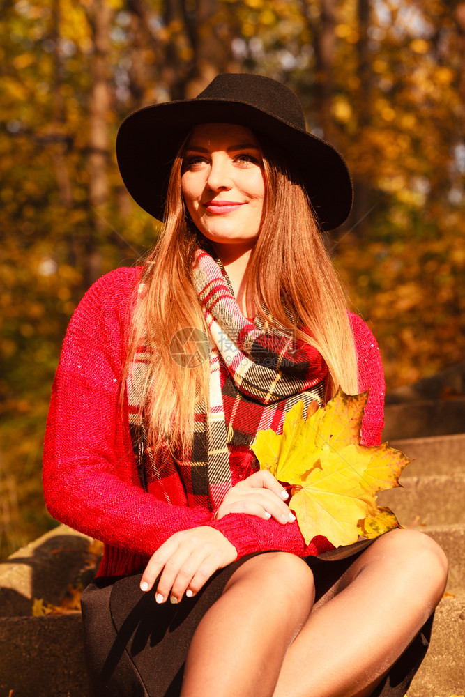 在秋天的公园里放松年轻时髦的黑帽子手拿着黄色的红树叶享受阳光秋天的女子在公园里放松图片