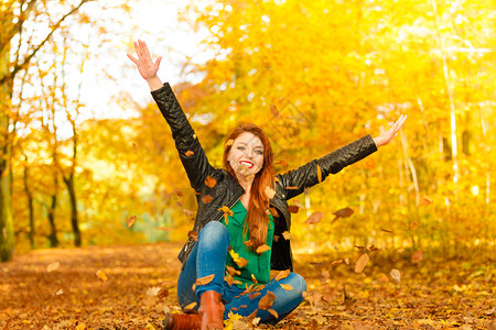 红头发女人在秋天的公园里放松将叶子扔在空中图片