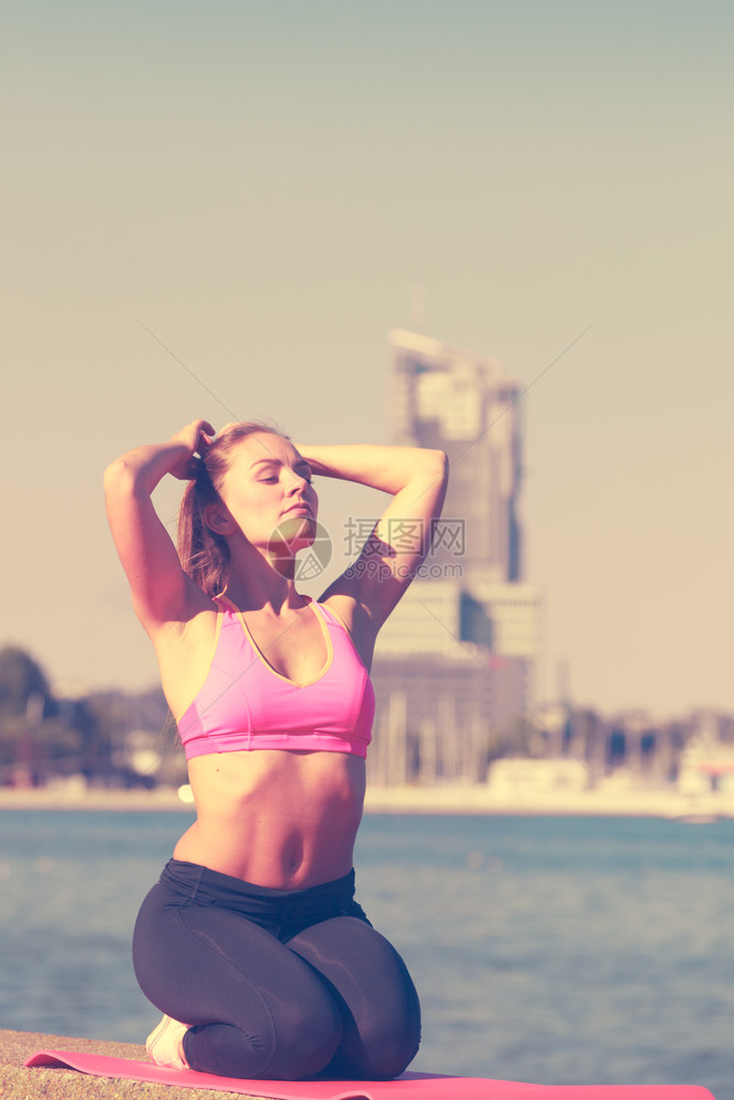 穿运动服的妇女坐在堤坝上锻炼前放松水和城市背景中放松图片