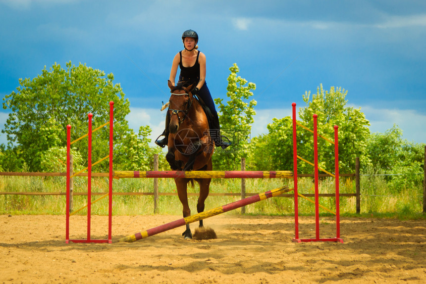 骑马的年轻女孩在阳光明媚的白天骑马跳过障碍的年轻女孩跳过障碍图片