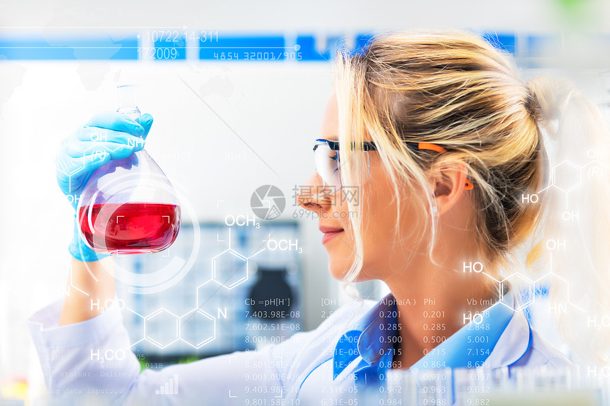 在化学研究实验室内带着保护眼镜和手套的装有红色液体物质的瓶子具有保护眼镜和手套的年轻快乐有吸引力的年轻女科学家图片