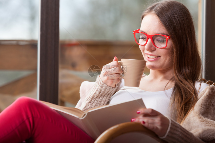 在家里坐摇椅上着舒适的年轻女士坐在摇椅上窗前客厅休息放松阅读书拿着咖啡杯坐在椅子上的妇女家里阅读书图片