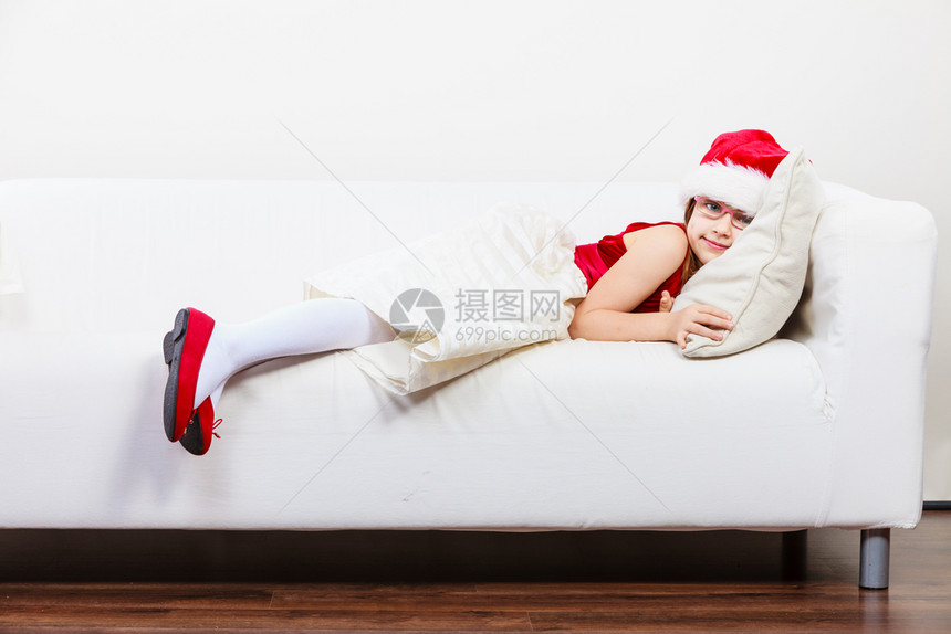 女孩在圣诞节时的家庭间可爱的小女人爬在沙发上小女人躺在沙发上休息时间穿着红色的圣达克萨斯帽子和鞋可爱的小女人爬在沙发上图片