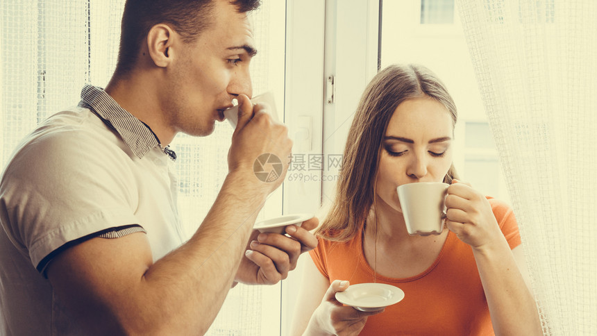 有吸引力的情侣在家中一起喝茶或咖啡男人和女在家中端杯子和热饮图片