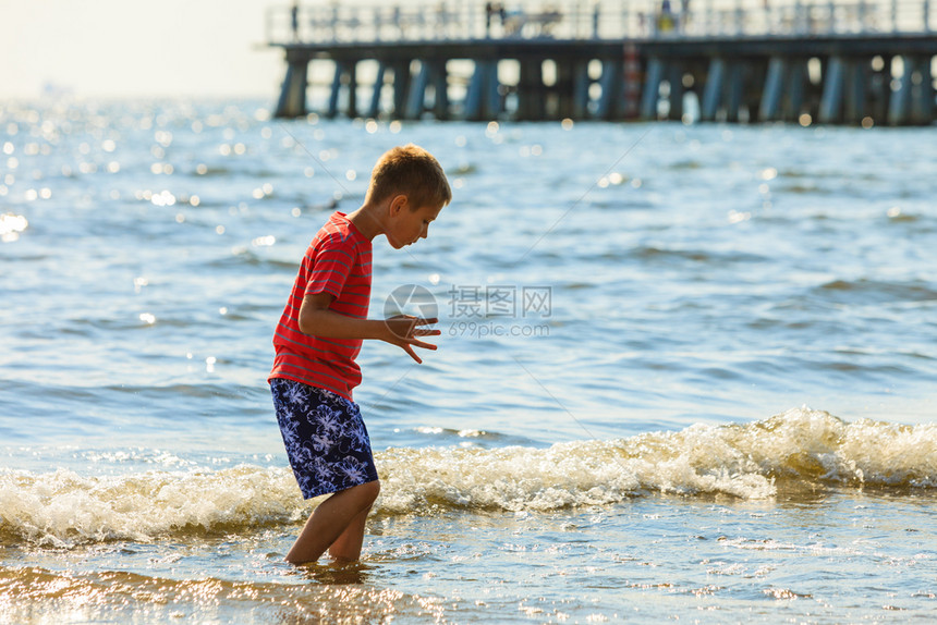 外面水的乐趣和欢男孩在海中走过孤独的孩子穿着夏衣在户外玩耍男孩在海滩上走过图片