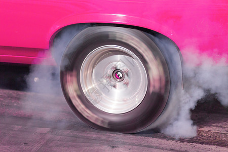 一辆粉红色的波迪种族赛车在前暖轮胎比赛前从燃烧的橡胶中制造烟雾图片