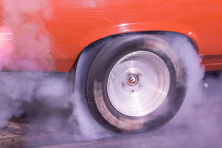 一辆橙色波丁种族赛车在跑前暖轮胎比赛前从燃烧的橡胶中制造烟雾图片